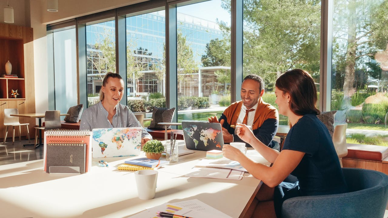 Three colleagues brainstorming with laptops in a well-lit office.